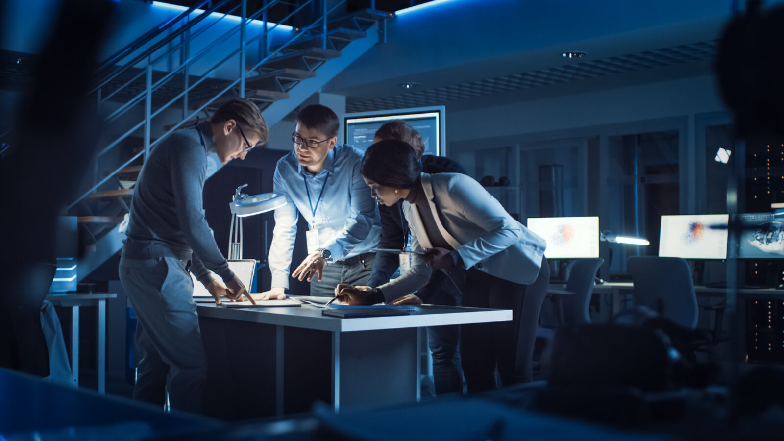 Diverse Team of Electronics Development Engineers Standing at the Desk Working with Documents, Solving Project Problems Late at Night. Specialists Working on Ultra Modern Industrial Design.